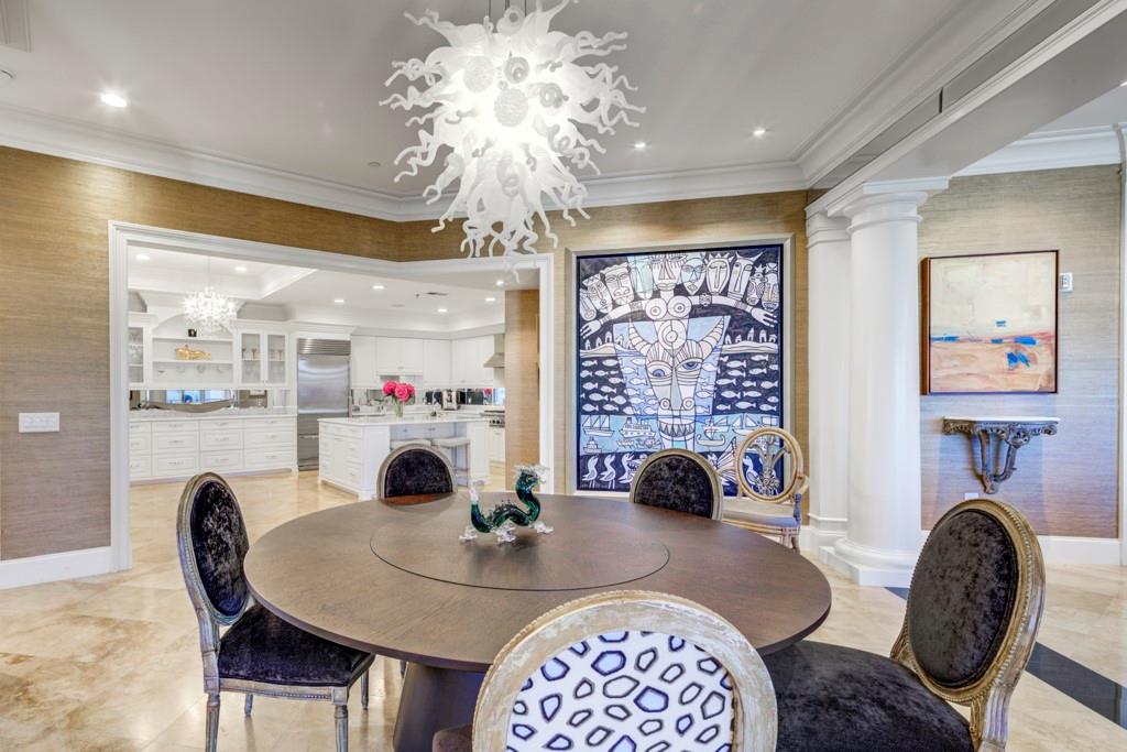 Dining room with a round table, sculptural chandelier, blue-and-white artwork, and an adjoining white kitchen.