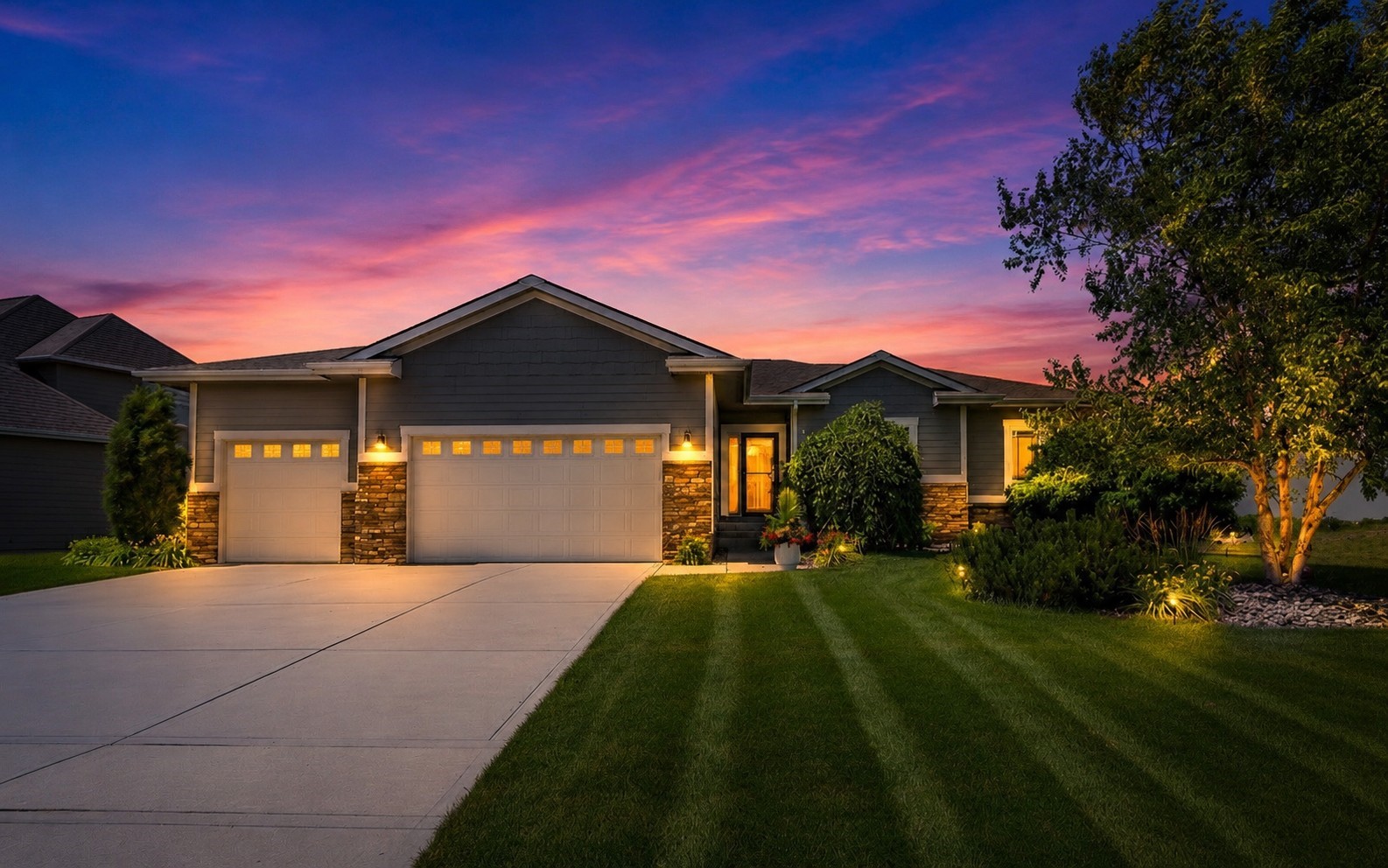 Single-story gray home with stone accents and a two-car garage beneath a vivid sunset.