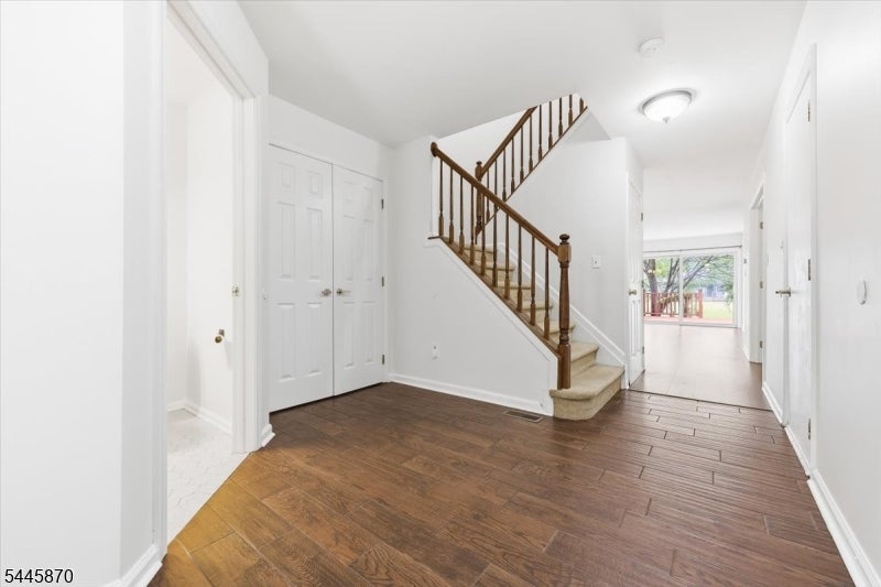 Entry foyer with a wooden staircase, dark hardwood flooring, and a view through to the backyard.