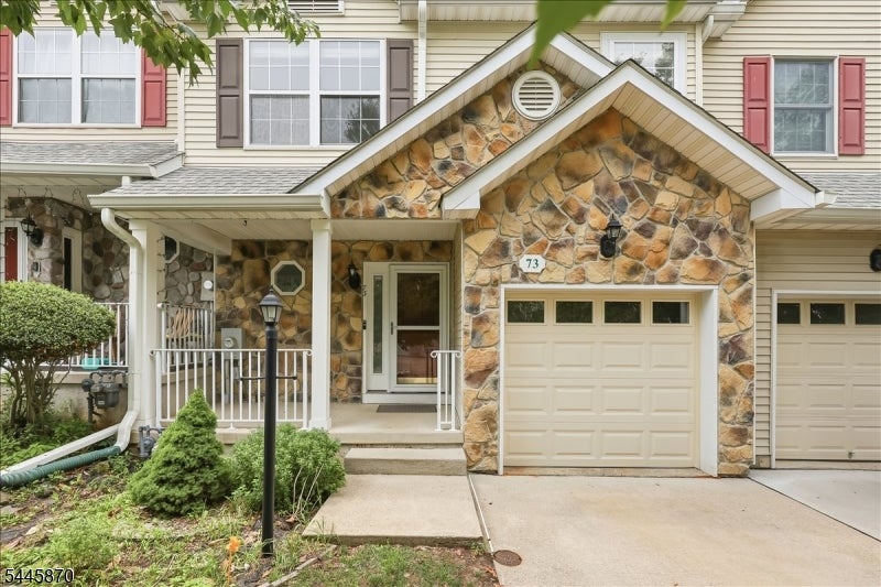Front exterior of 73 Castleton Rd, with a stone entry facade, garage, and covered porch.