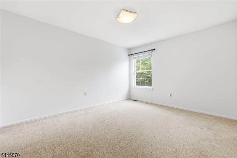 Empty bedroom with beige carpeting and a window overlooking greenery.