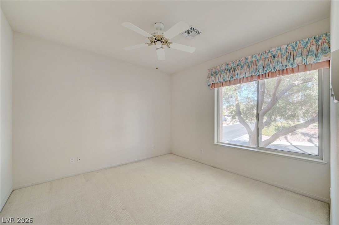 Empty carpeted bedroom with a ceiling fan and large window beneath a colorful valance.