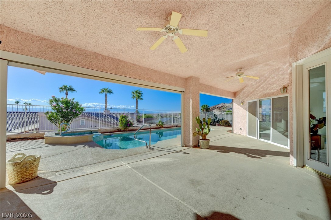 Covered patio overlooking a pool, with ceiling fans and distant mountains beyond the railing.