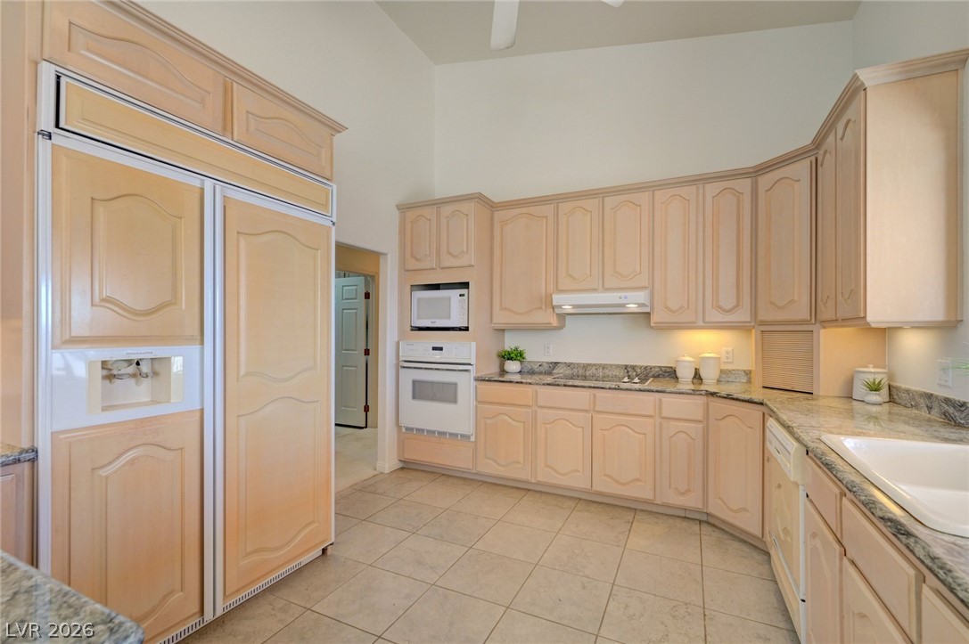 Kitchen with pale wood cabinetry, granite counters, built-in refrigerator, and tiled floor.