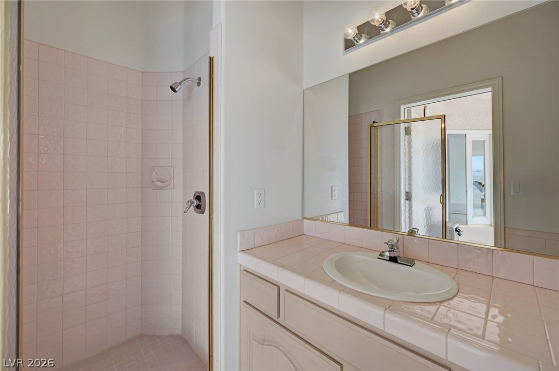 Bathroom with a pink tiled shower and matching vanity beside a large mirror.