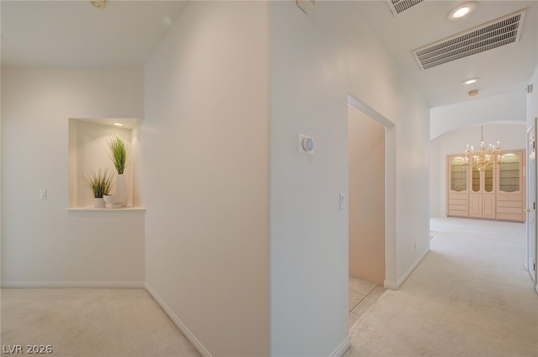 Carpeted hallway with a recessed plant niche and a chandelier over cabinets in the adjoining room.