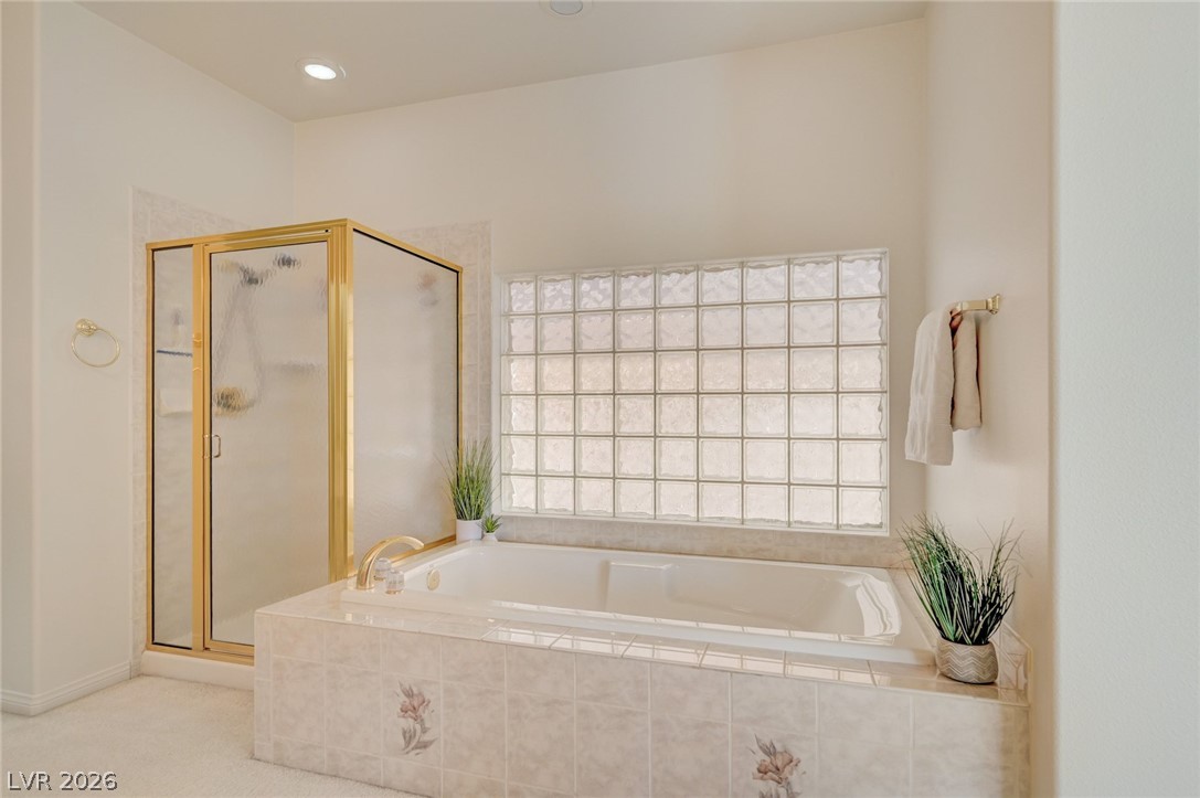 Bathroom with a built-in soaking tub beneath a glass-block window and a gold-trimmed shower.