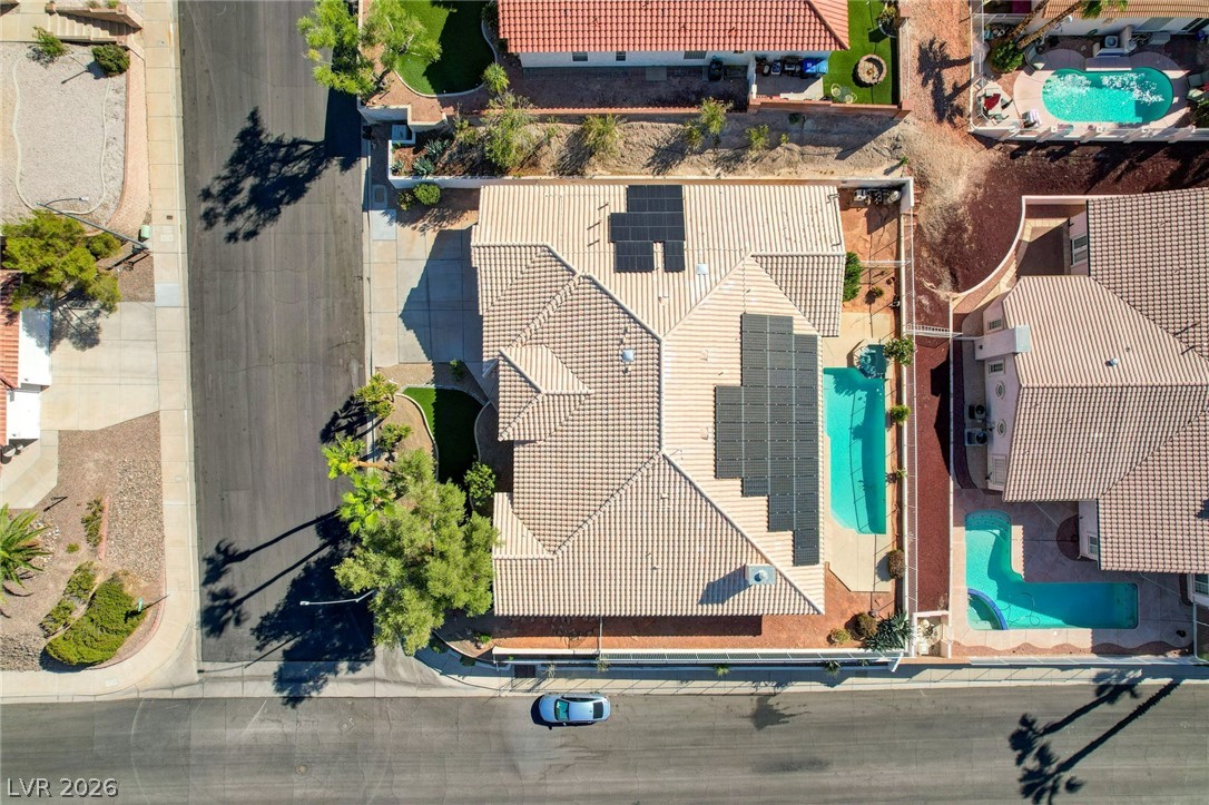 Aerial view of a tiled-roof home with rooftop solar panels and a narrow side-yard pool.