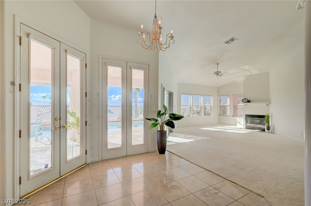 Vacant living room with tiled floors, a chandelier, fireplace, and glass doors overlooking the pool.