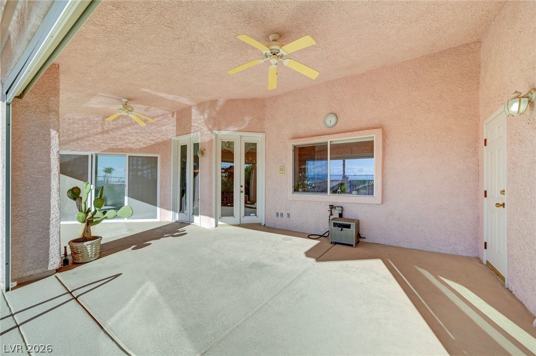 Covered patio with pink stucco walls, two ceiling fans, sliding glass doors, and a potted cactus.