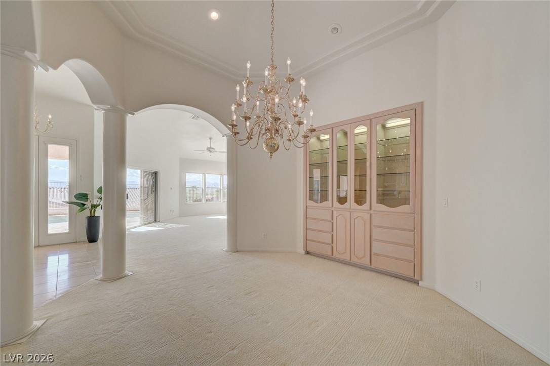 Formal dining room with a chandelier, built-in glass-front cabinets, and arched openings to the living area.