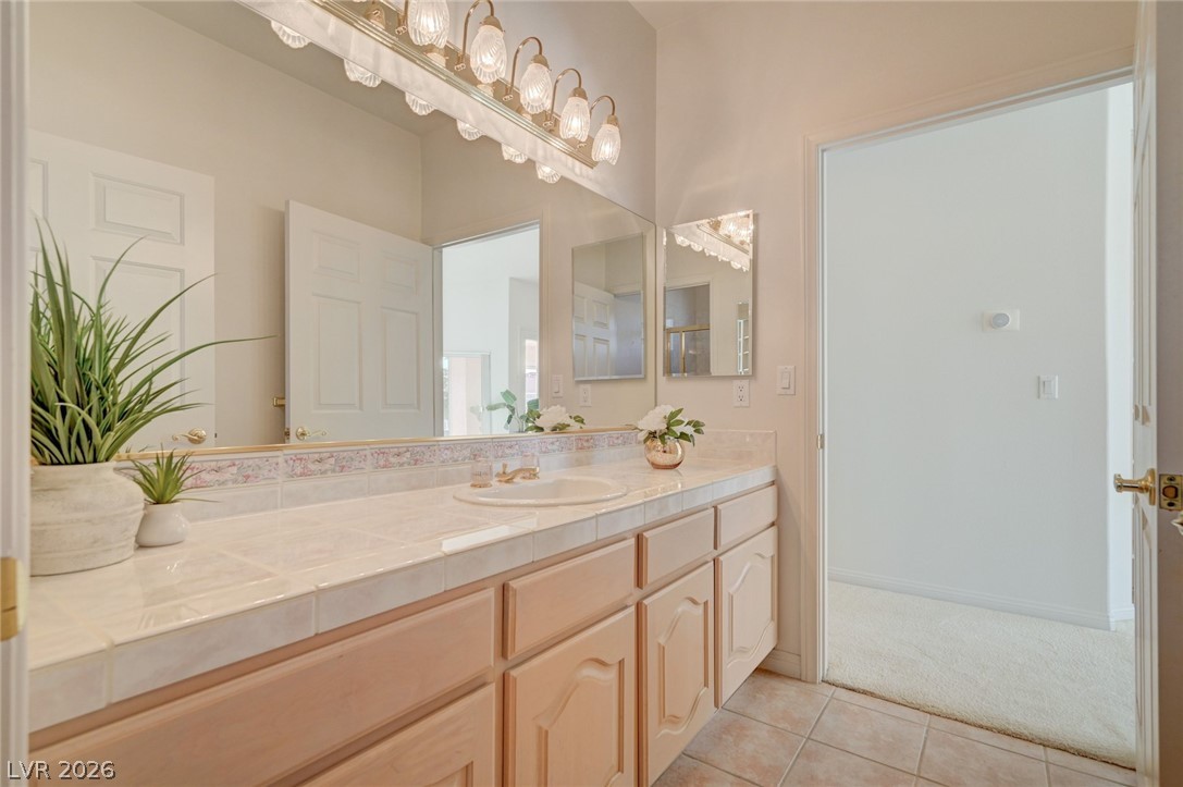 Bathroom vanity with tiled countertop, light wood cabinets, large mirror, and bright vanity lights.