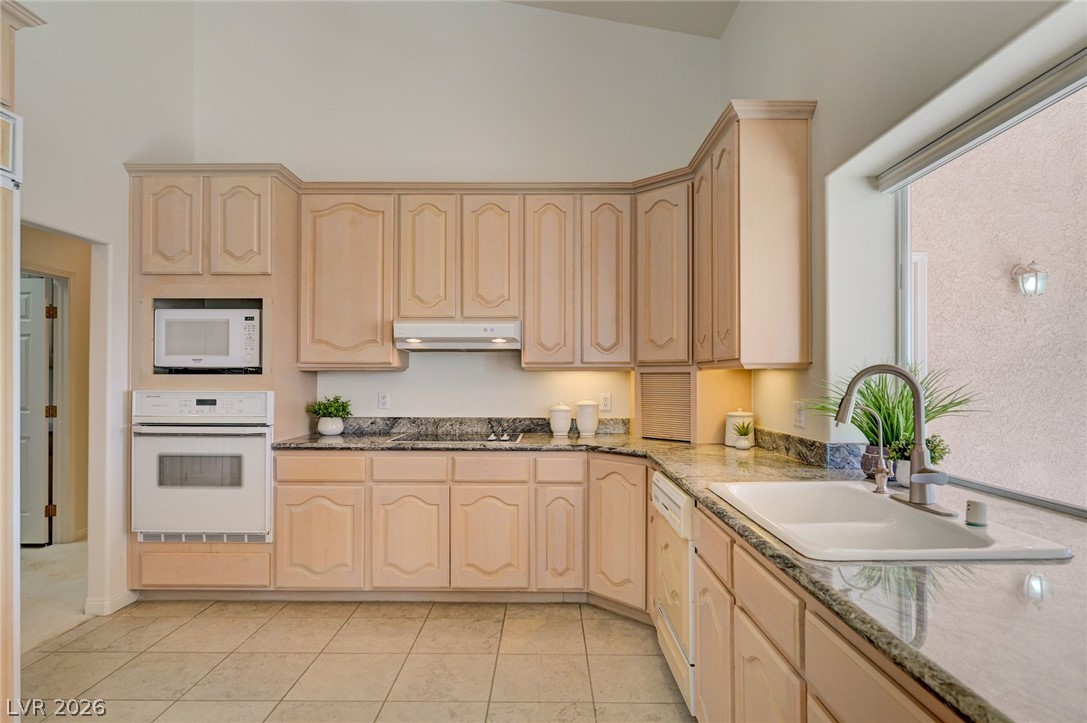 Kitchen with light wood cabinets, granite counters, and a white sink beneath a large window.