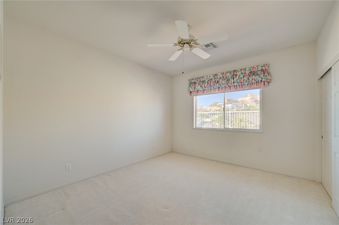 Empty carpeted bedroom with a ceiling fan and a window overlooking nearby hills.