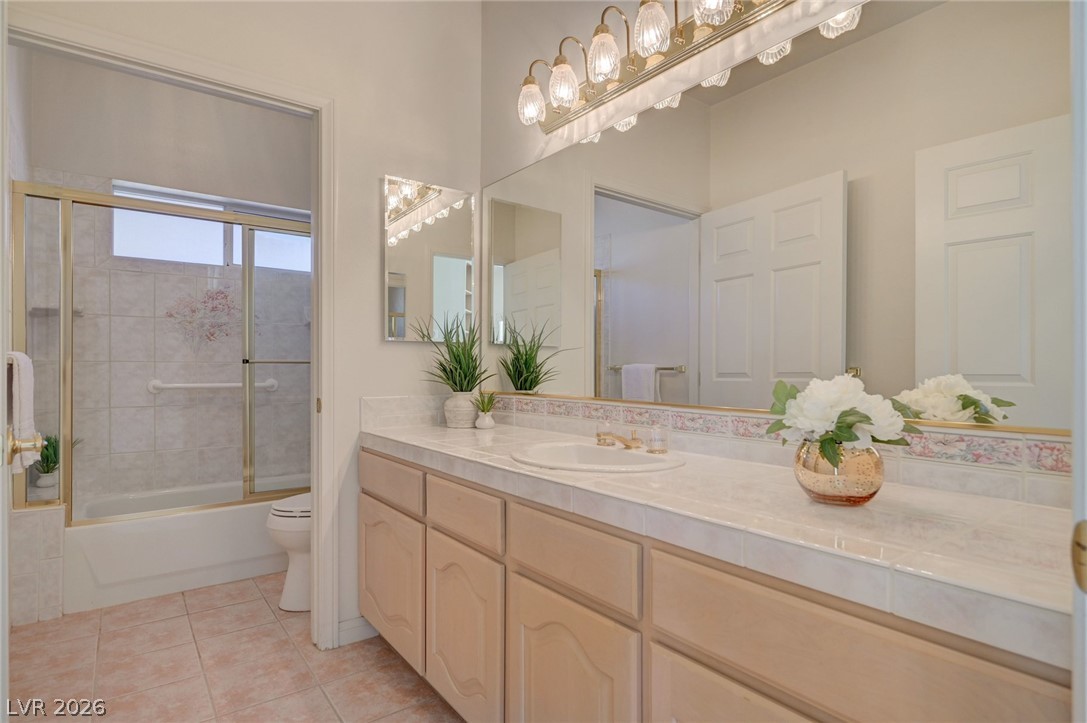 Bathroom with a long pale-wood vanity, sliding glass shower door, and white flowers on the counter.