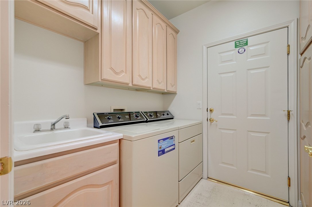 Laundry room with a washer and dryer beside a utility sink and pale cabinets.