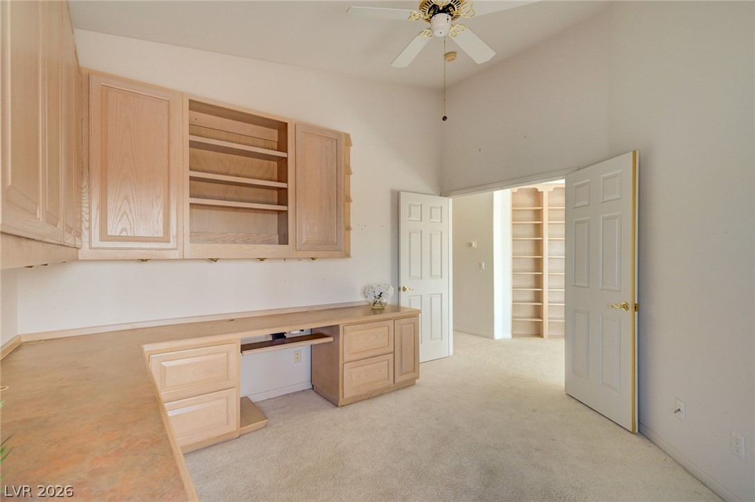 Home office with light wood built-in desk and cabinets, opening to a room with shelving.