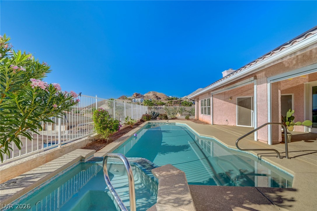 Backyard pool and attached spa beside a pink stucco home, with rocky hills in the distance.