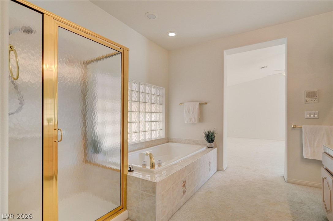 Bathroom with a tiled soaking tub, glass-block wall, and gold-framed frosted-glass shower.