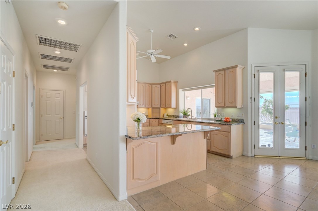 Kitchen with light wood cabinetry, granite counters, a large peninsula, and French doors facing the pool.