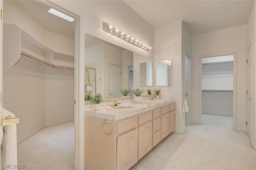 Bathroom with a long double-sink vanity and open walk-in closets on both sides.