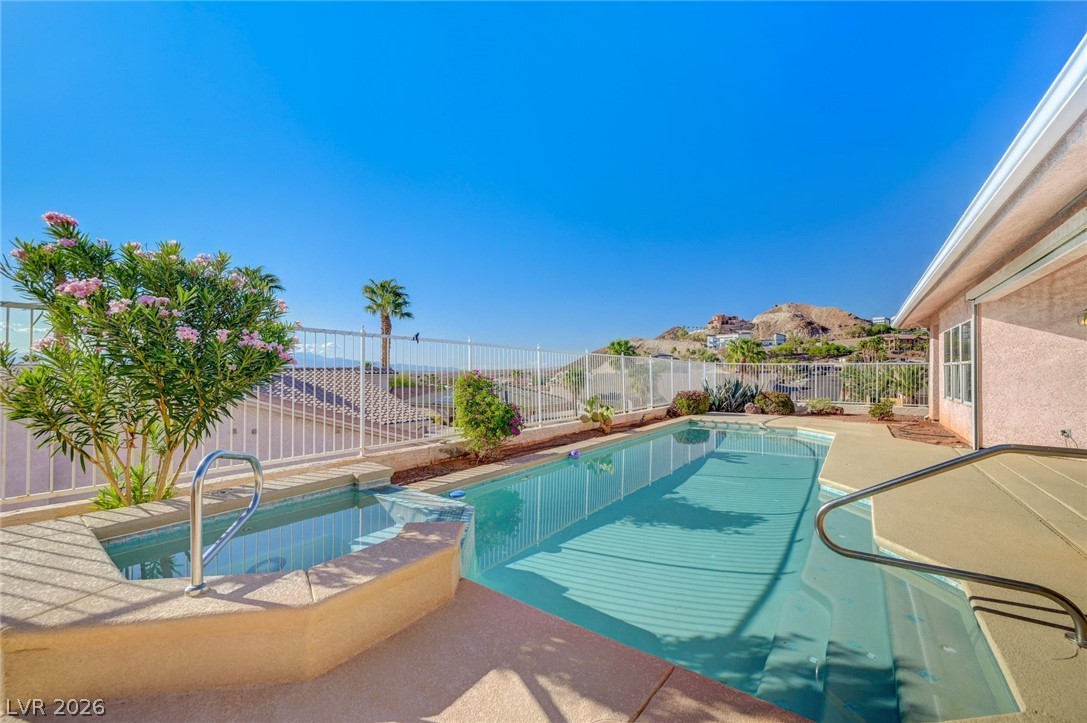 Backyard swimming pool and raised spa with desert hills beyond a white fence.