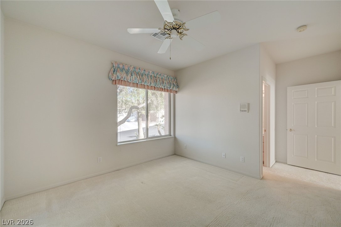 Empty carpeted bedroom with a ceiling fan and a window topped by a patterned valance.