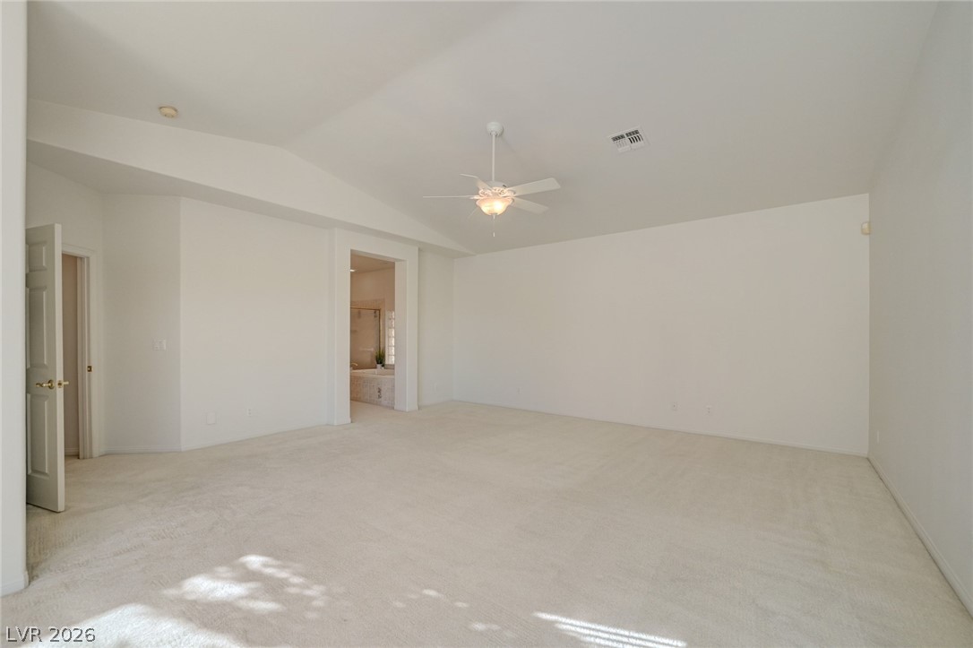 Empty carpeted bedroom with a ceiling fan and an open doorway to a bathroom.