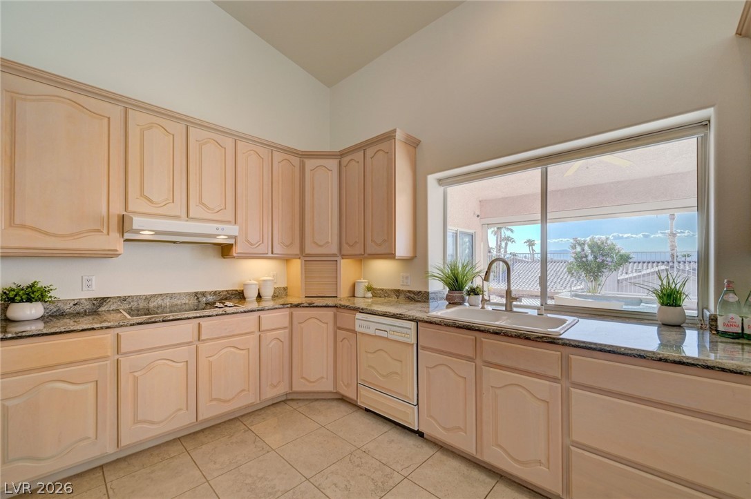 Kitchen with light wood cabinets and granite counters, looking out to a covered patio through a large window.