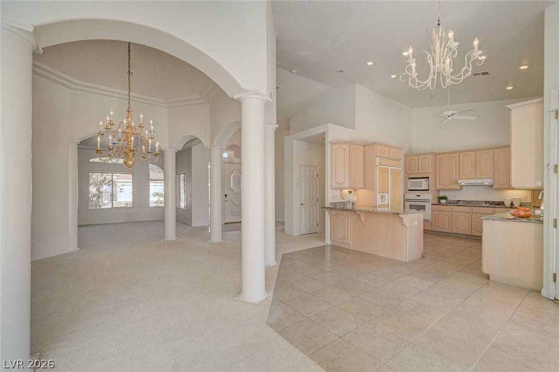 Open living and dining area with arched columns, chandeliers, and a light wood kitchen island.