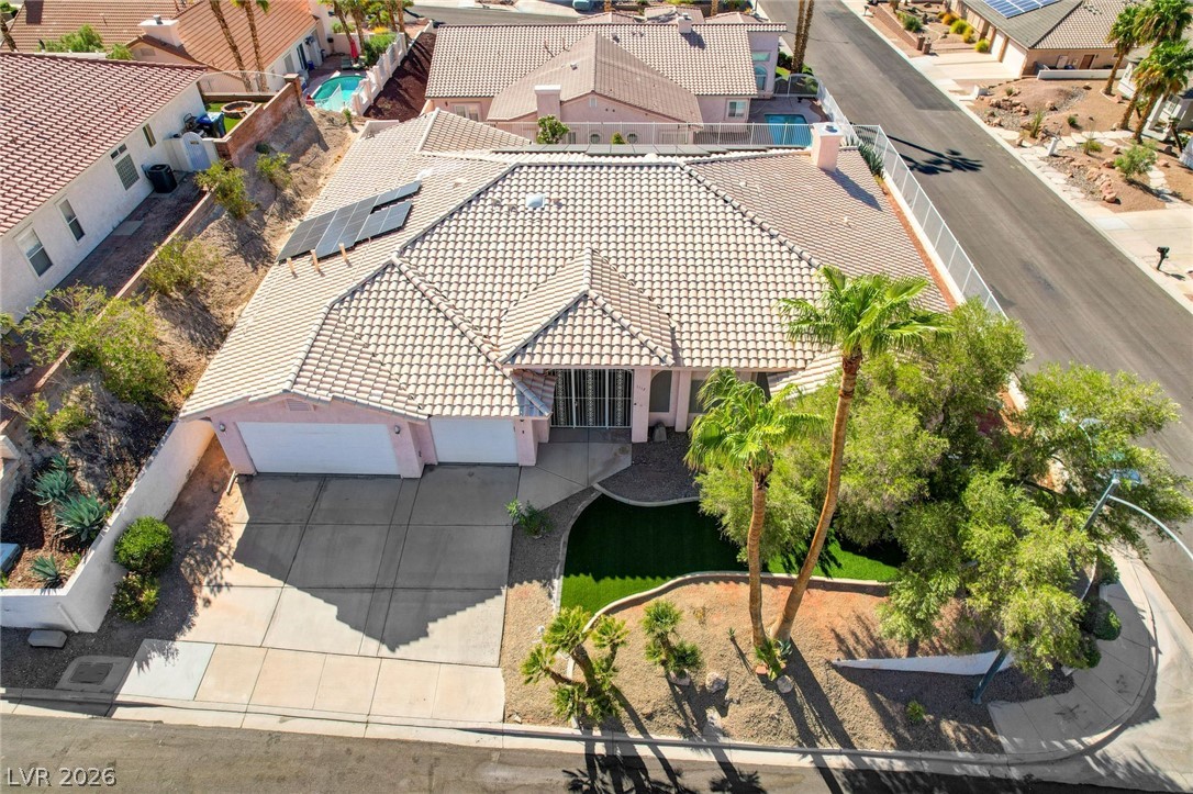 Aerial view of a tiled-roof home with solar panels, a two-car garage, and a palm-lined yard.