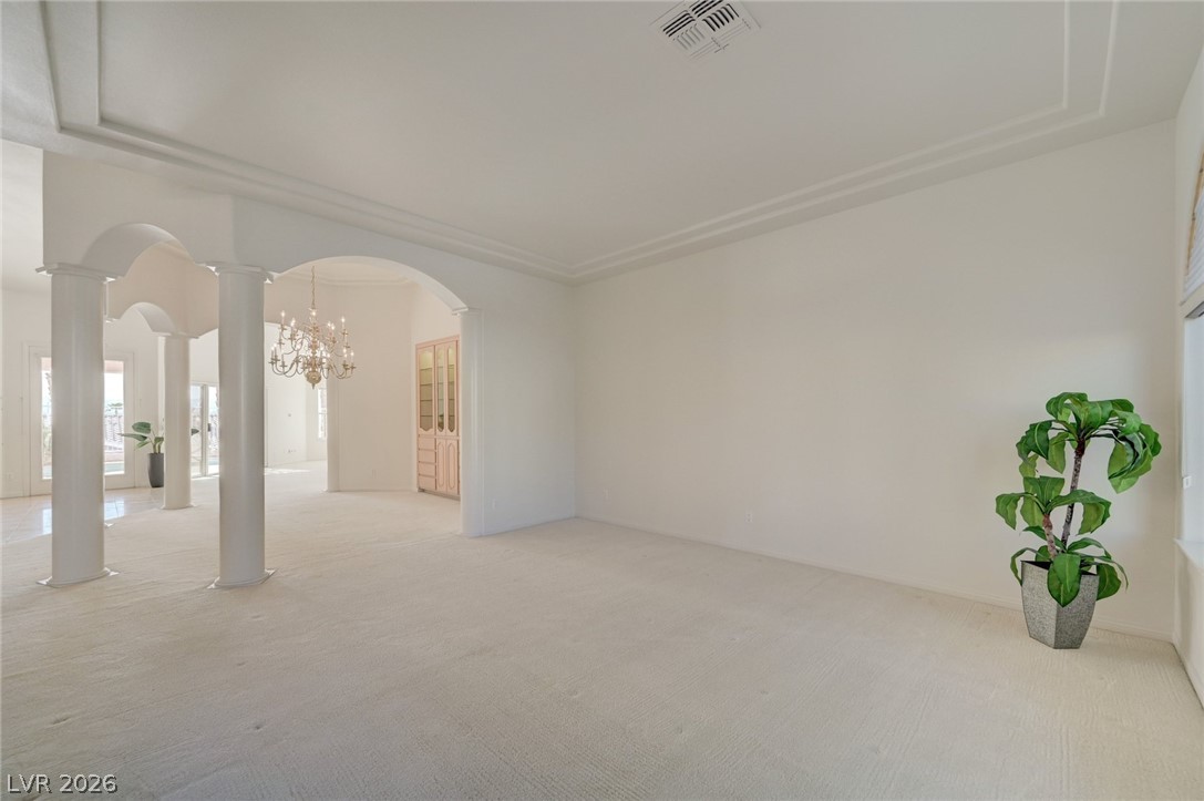 Carpeted living area with arched openings, white columns, and a chandelier.
