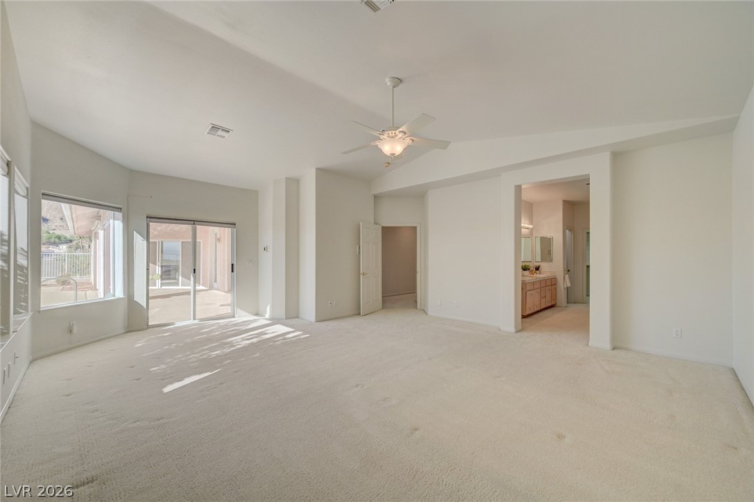 Empty carpeted living room with a ceiling fan and sliding glass doors opening to a patio.