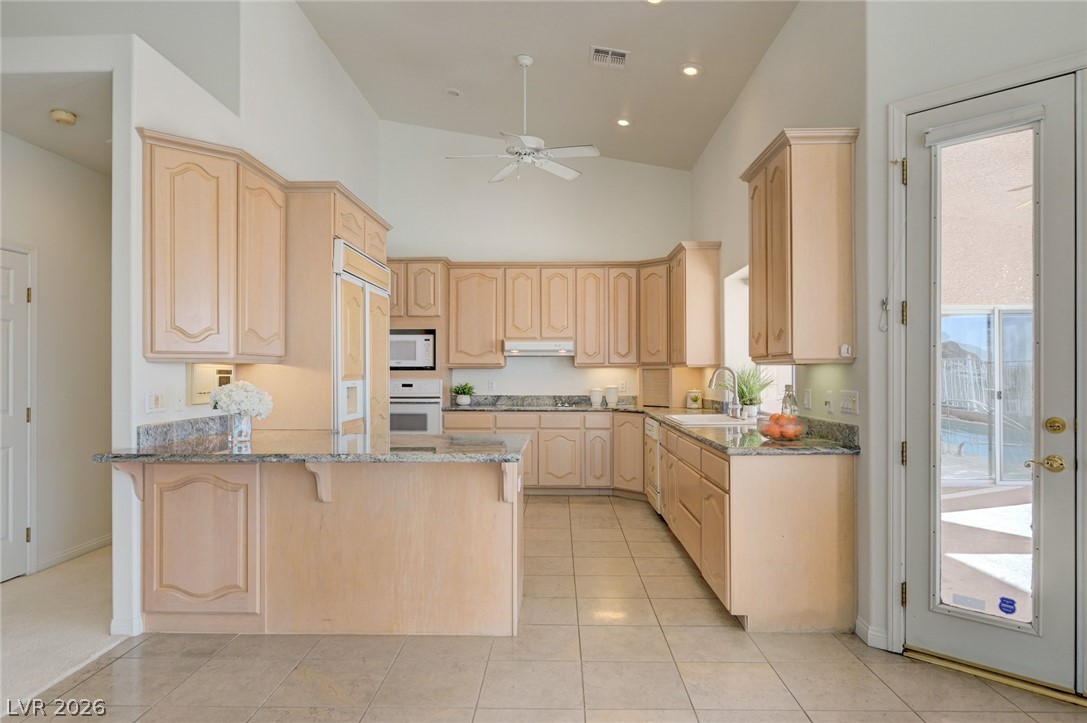 Kitchen with light wood cabinets, granite counters, and a glass door overlooking the pool.