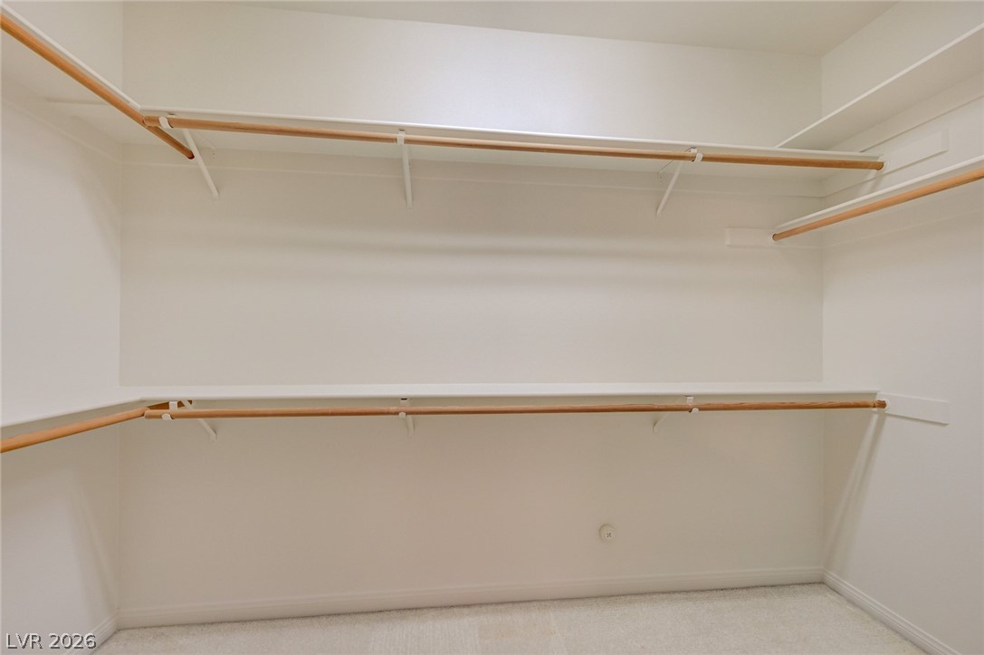 Empty walk-in closet with wooden hanging rods and shelves along three sides.