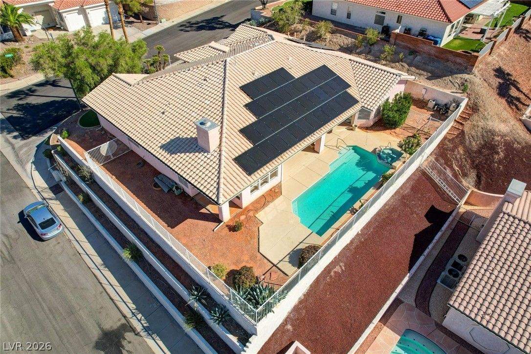 Aerial view of a tile-roofed home with solar panels and a backyard swimming pool.