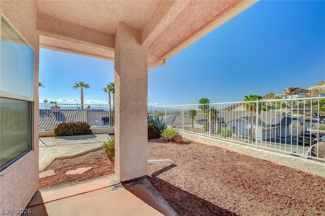 Covered patio overlooking nearby homes and rocky hills, with a white railing and desert landscaping.