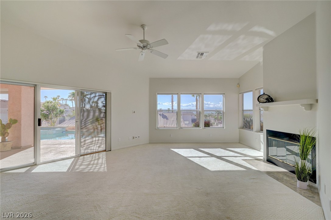 Vacant living room with a fireplace, broad windows, and sliding doors overlooking a pool.