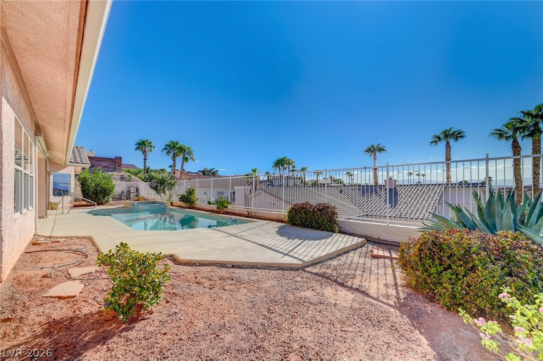 Backyard pool beside a wide patio, desert landscaping, and a metal fence.