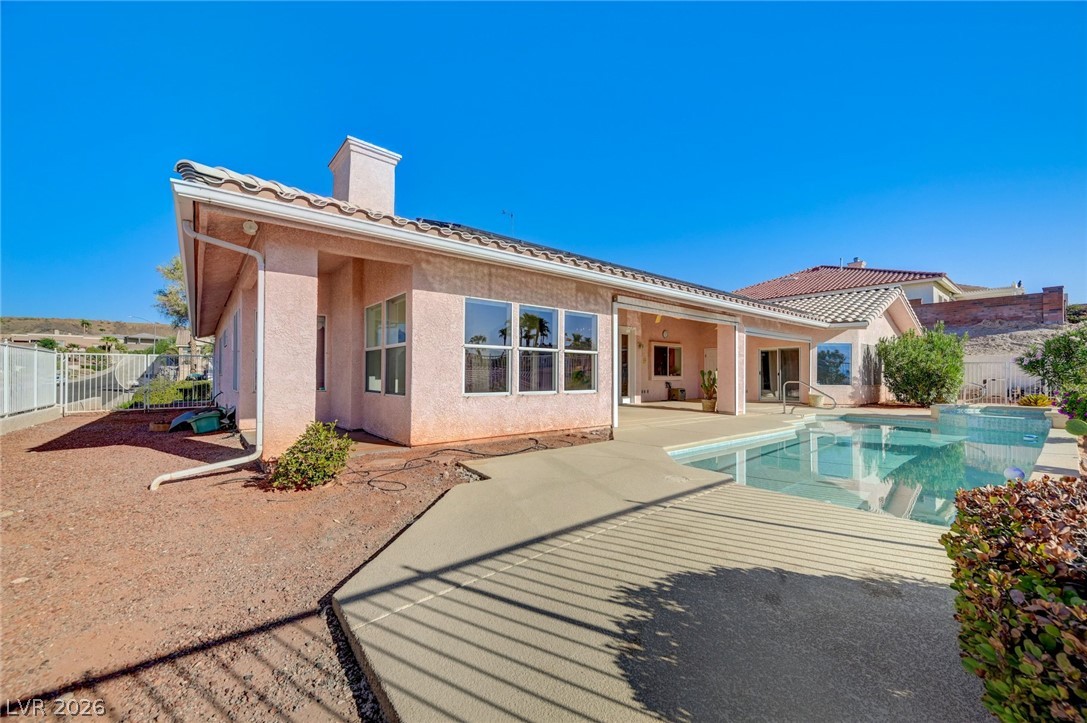 Rear of a stucco home with a covered patio and swimming pool.