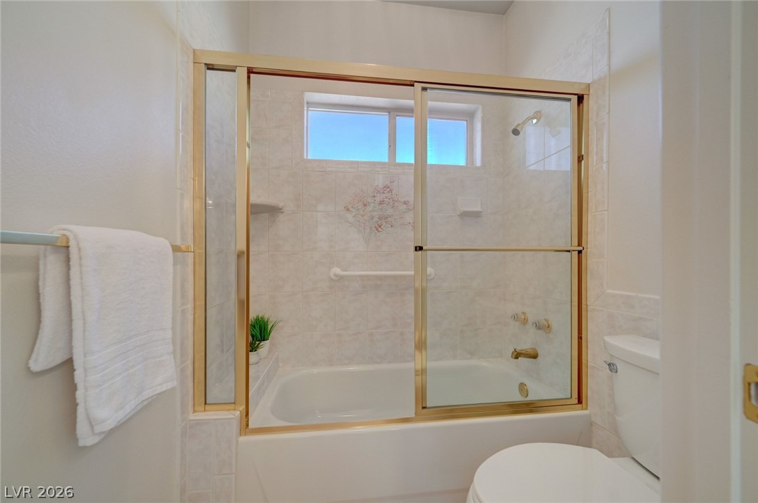 Bathroom with a white tub, gold-framed sliding glass doors, tiled walls, and a high window.