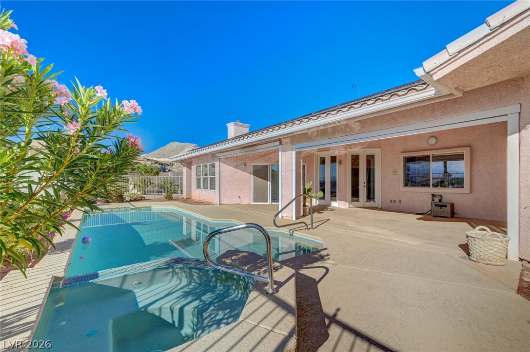 Backyard pool beside a pink stucco home, with a broad patio and flowering shrubs.