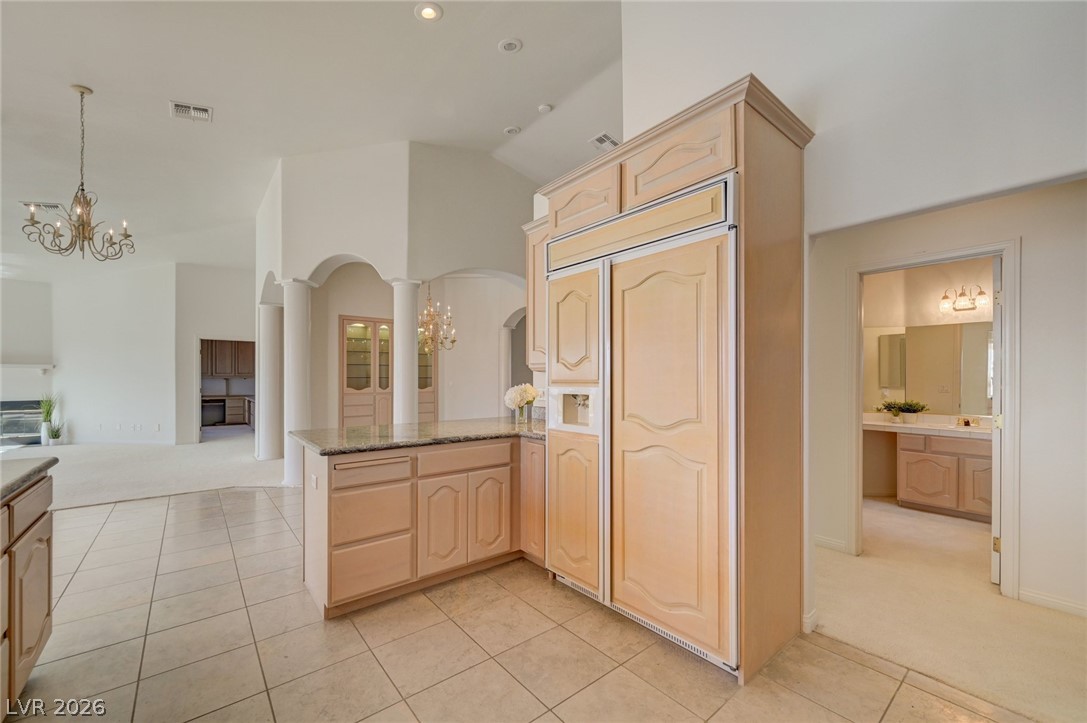 Kitchen with light wood cabinetry, built-in refrigerator, granite island, and tile floors.