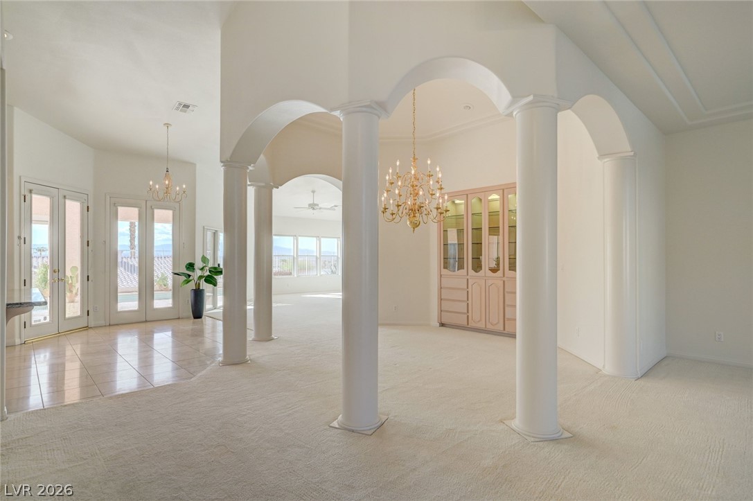 Vacant living room with white columns, arched openings, chandelier, and built-in display cabinet.
