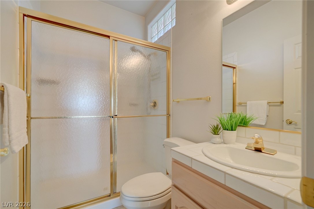 Bathroom with a frosted-glass shower, tiled vanity, and gold-tone fixtures.