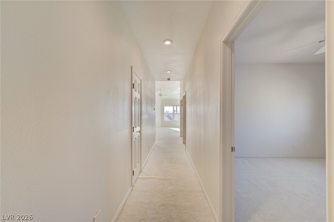 Carpeted hallway with recessed lights and an open doorway to an empty room.
