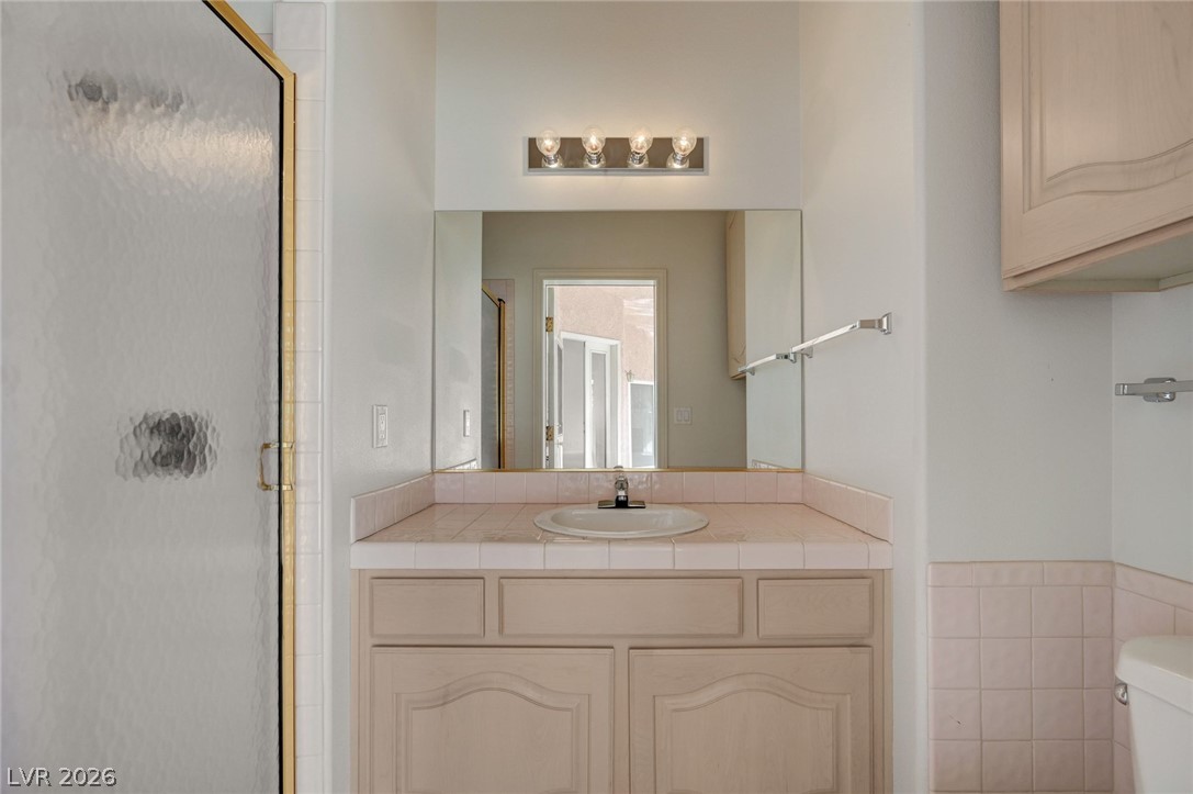 Bathroom vanity with pink tile countertop, large mirror, and glass shower enclosure.