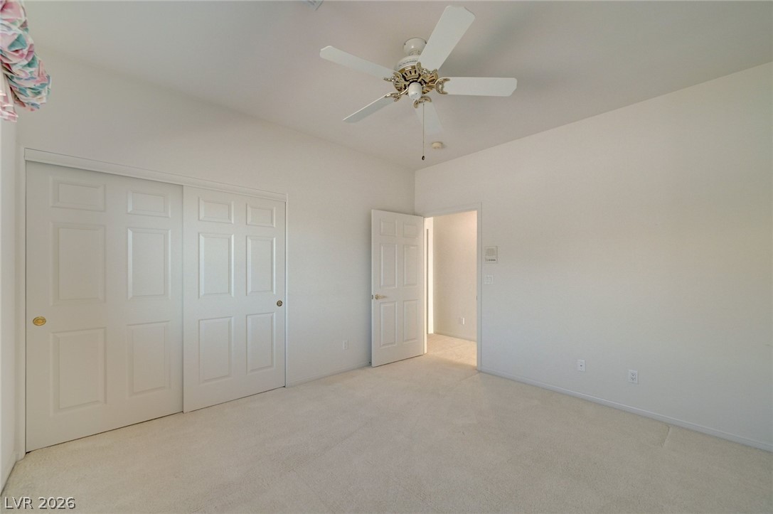 Vacant bedroom with white closet doors, light carpet, and a ceiling fan.