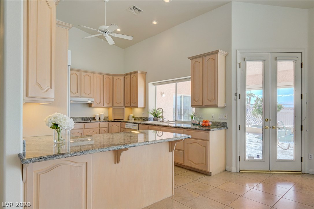 Kitchen with pale wood cabinetry, granite counters, and glass doors overlooking a pool patio.