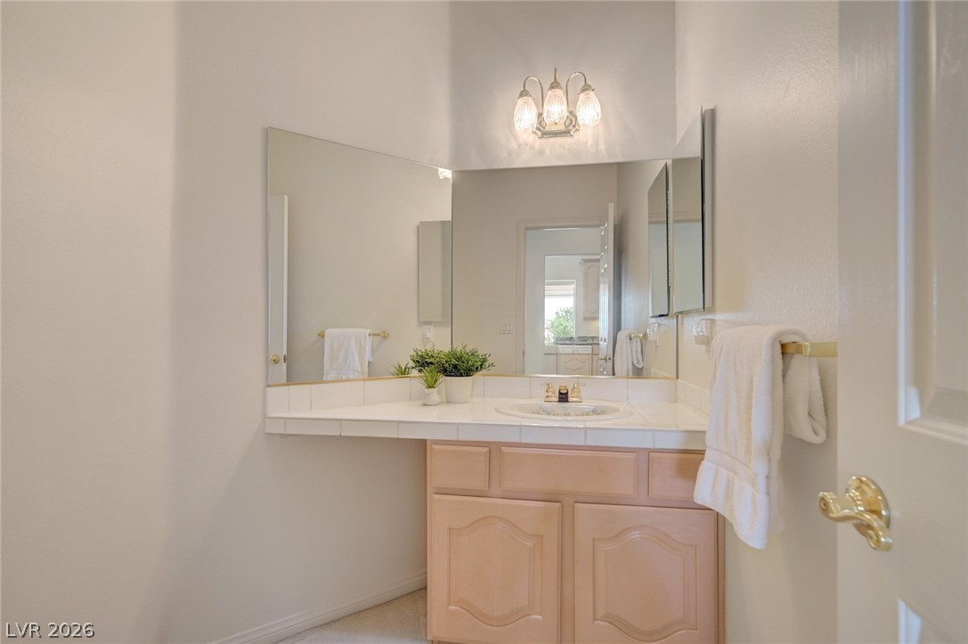 Bathroom vanity with a large mirror, white tiled counter, and light wood cabinets.
